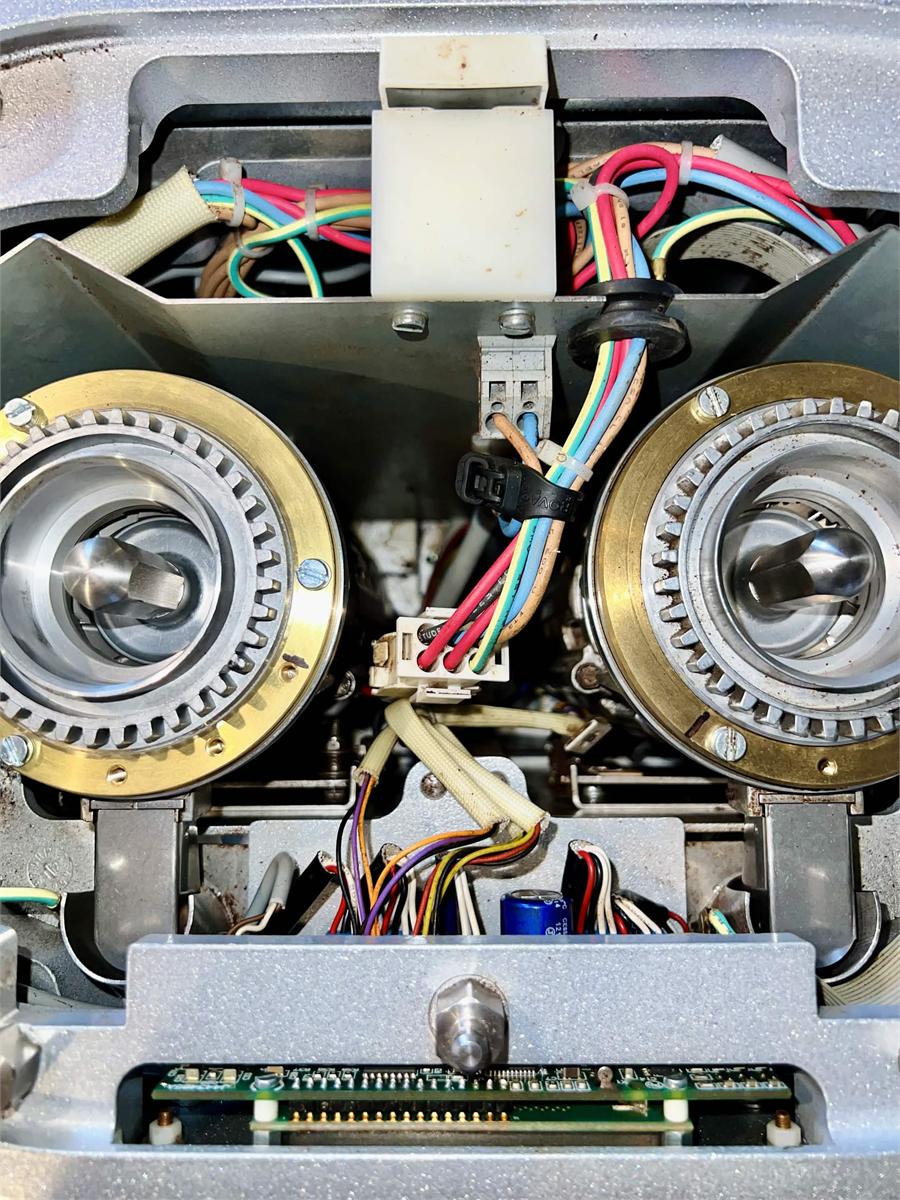 A twin espresso grinder opened on the bench, both burr carriers and internal wiring exposed